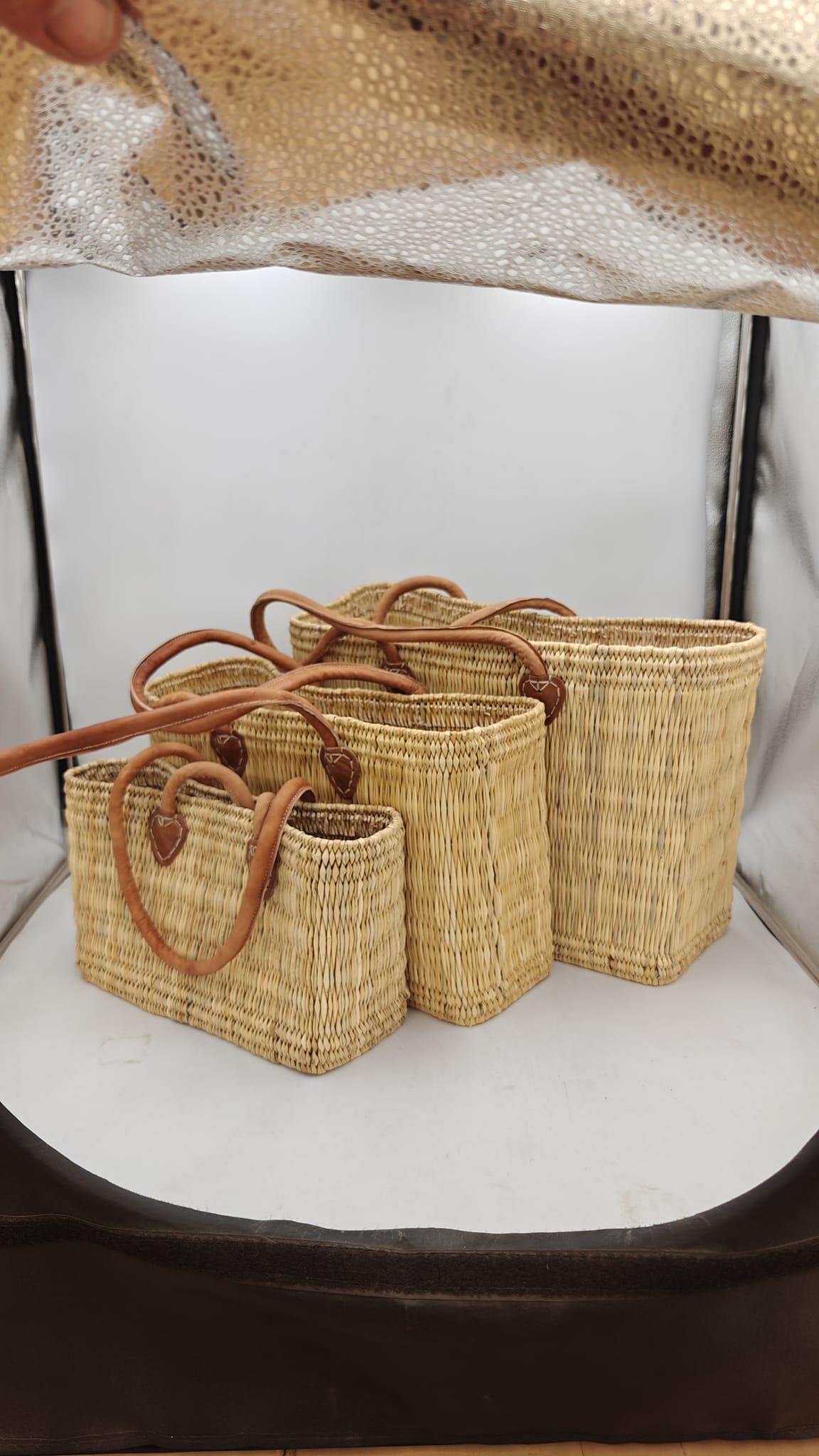 Tres capazos de esparto natural con asas de cuero en tamaños pequeño, mediano y grande, fotografiados en estudio sobre fondo blanco