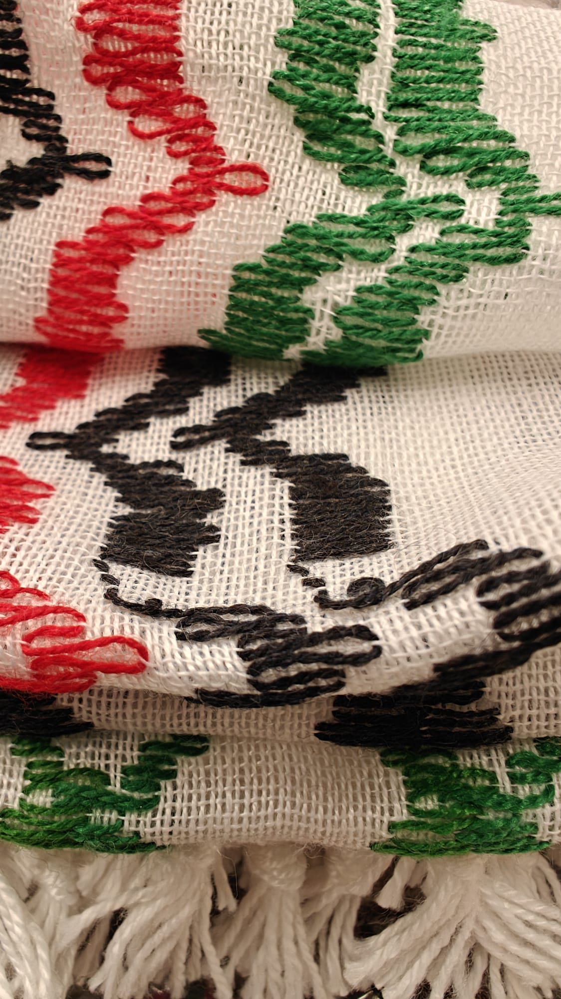 Primer plano del tejido de kufiya palestina con bordados en los colores de la bandera: negro, verde, rojo y blanco, flecos de algodón natural