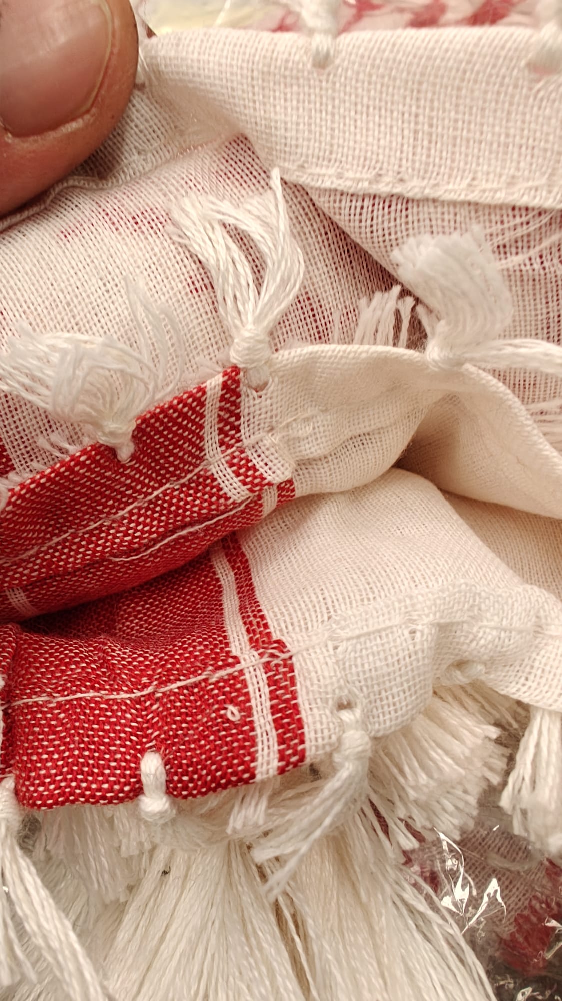 Primer plano del tejido de kufiya palestina rojo y blanco, textura algodón natural con flecos tradicionales, detalle de calidad artesanal