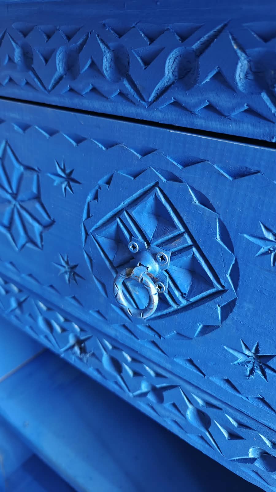 Detalle de cajón azul de madera tallada con rosetas geométricas y tirador de anilla
