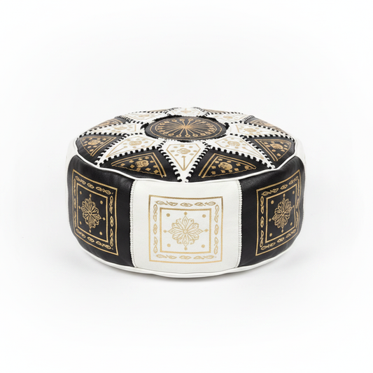 Puff marroquí artesanal de cuero negro y blanco con bordados dorados y patrón geométrico, sobre fondo blanco
